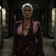 In her shiny maroon pantsuit, a serious Pamela Milton stands in The Commonwealth prison.